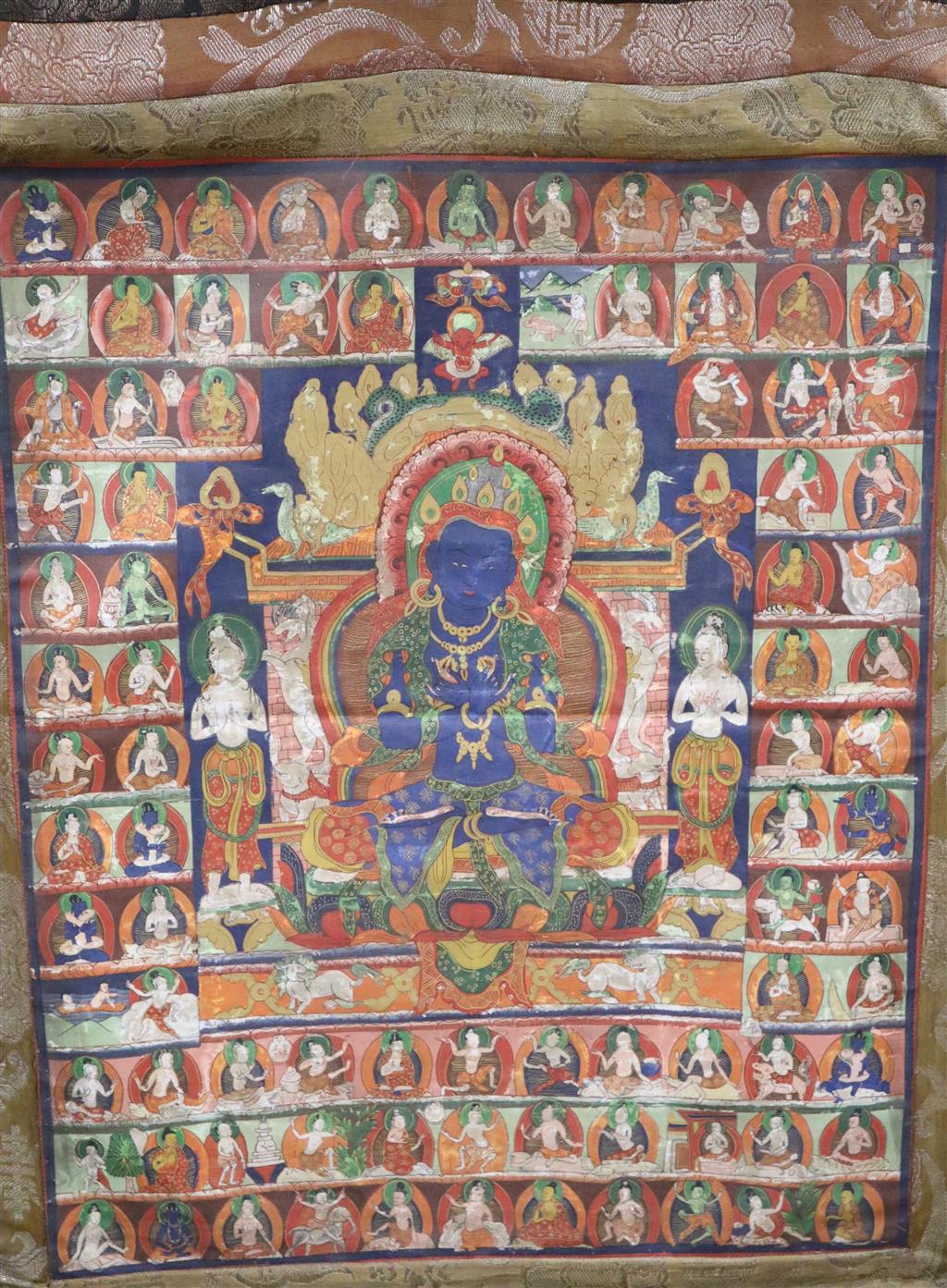 A Tibetan painted silk thangka with a blue Buddha surrounded by figures, central panel 54 x 43cm, overall 86 x 60cm